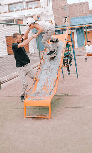 Volunteer helping a peruvian child dropping with her skateboard on a slide.