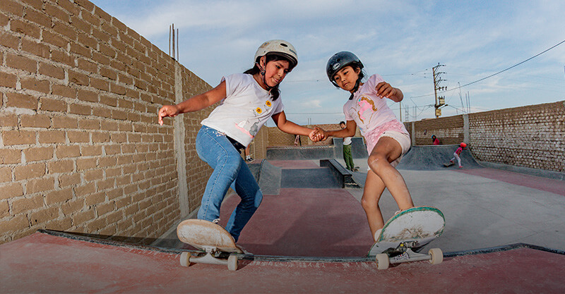 Two girls helping each other on a skateboard at the Cerrito's Skatepark in Peru.